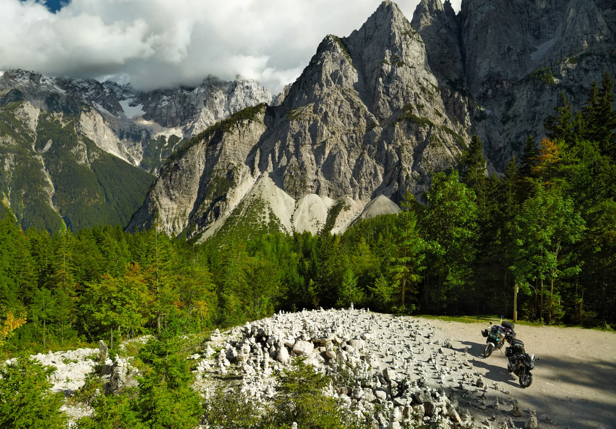 Two motorcycles on a cobblestone mountain road with jagged peaks in the background