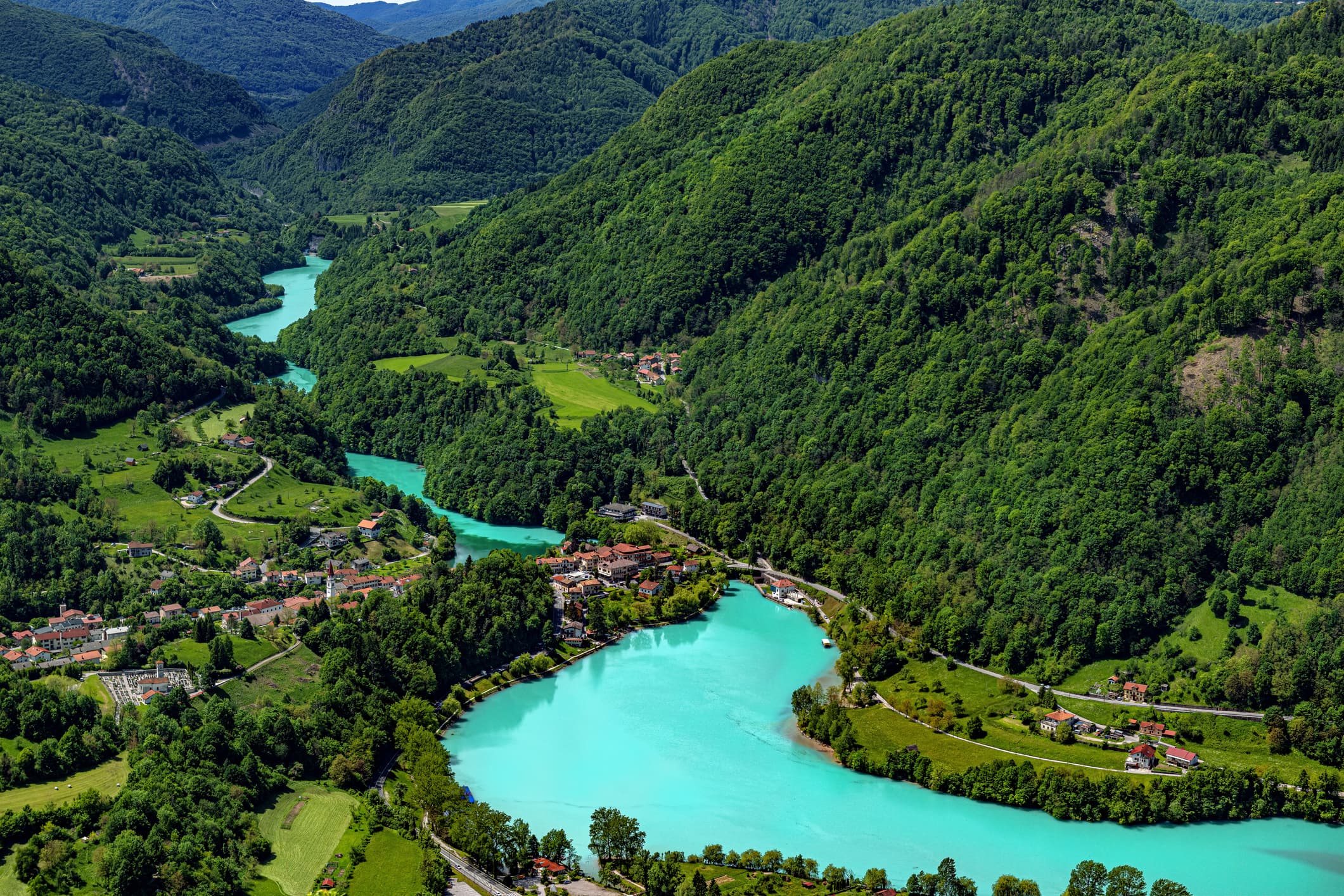 The turquoise Soča River winds through forested mountains, with a small village along its banks