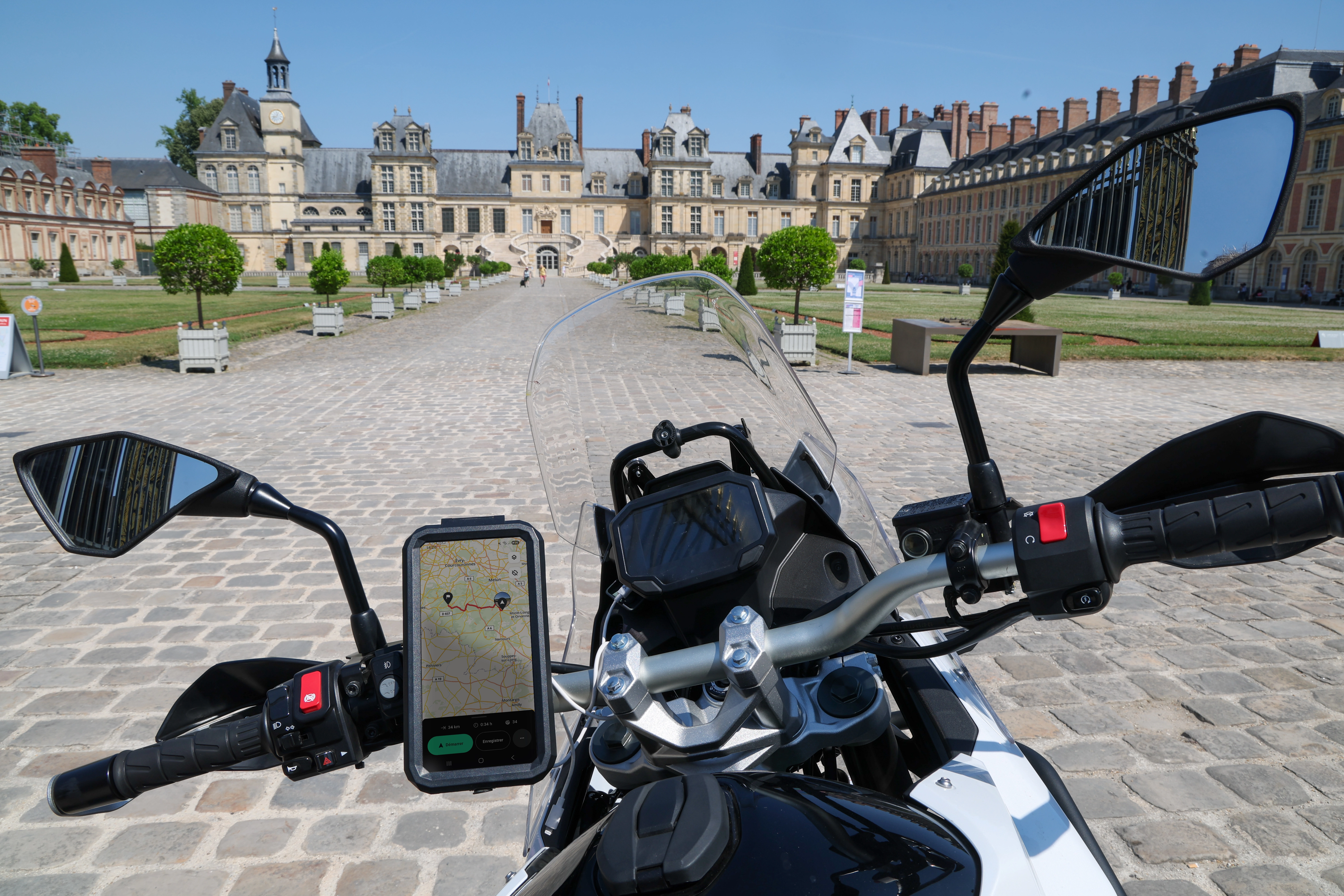 Un motard en tenue de protection est assis sur une moto Triumph sur une route forestière sinueuse, avec des informations de navigation et d'itinéraire affichées ainsi que le slogan « <b>Planifiez facilement</b><br>
vos balades à moto sur <br>routes sinueuses ! ».